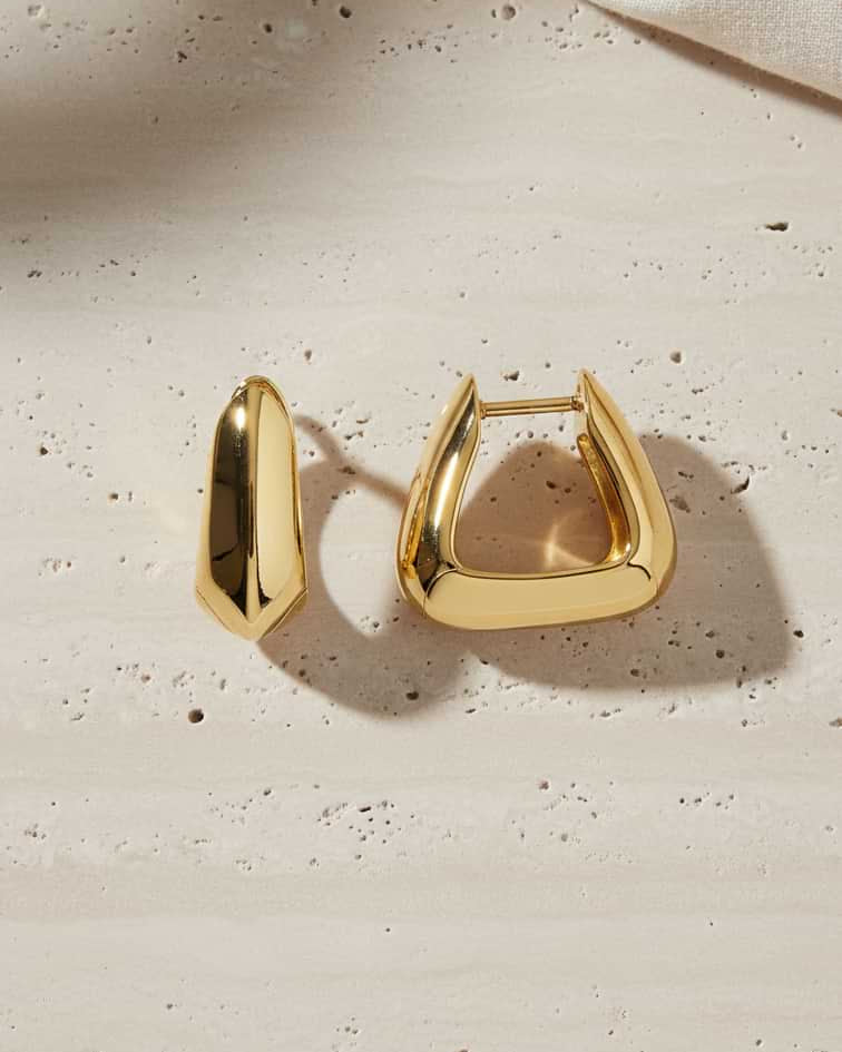 Gold triangle hoop earrings on a textured beige surface