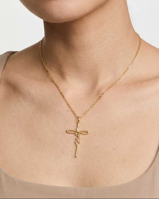 Woman wearing a gold necklace with a love scripted pendant on a plain background