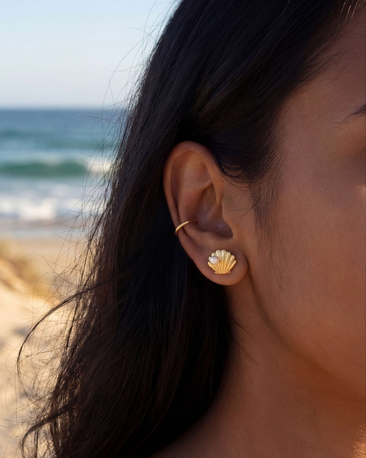 Woman wearing a gold shell stud earring with a beach background