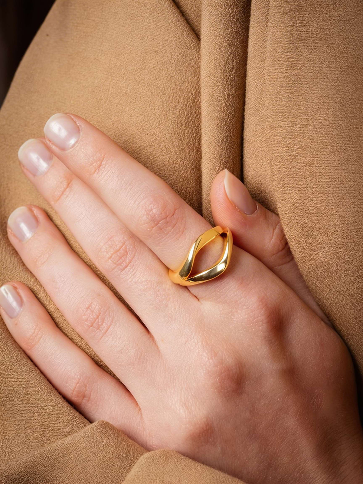 Two mirrored gold rings on a hand with a camel fabric background