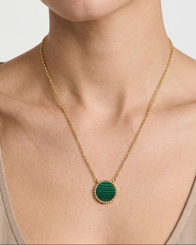 A close-up of a model wearing a delicate gold chain necklace with a round green malachite stone and beaded pendant.