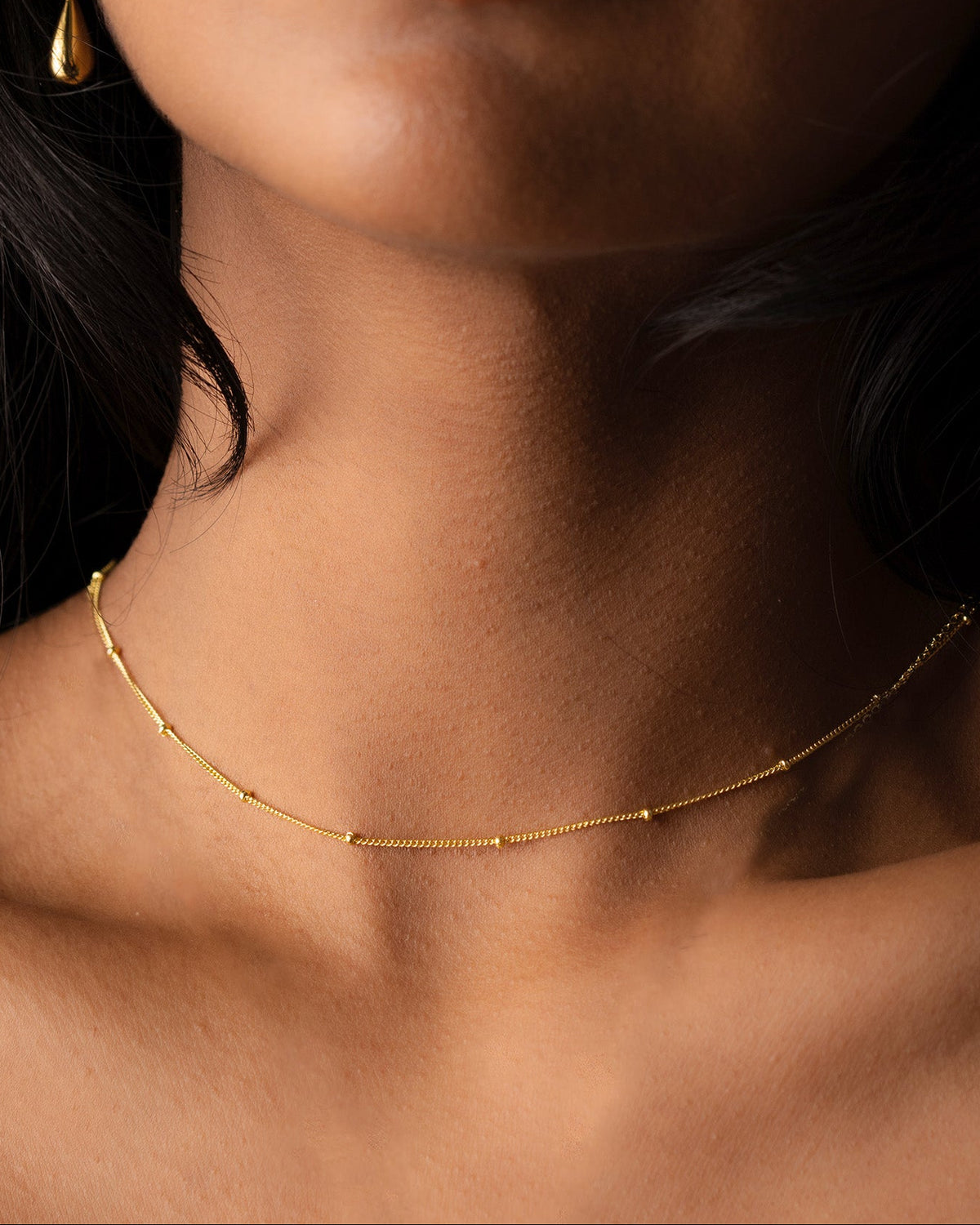 Close-up of a woman wearing a gold fine beads necklace with a dark background