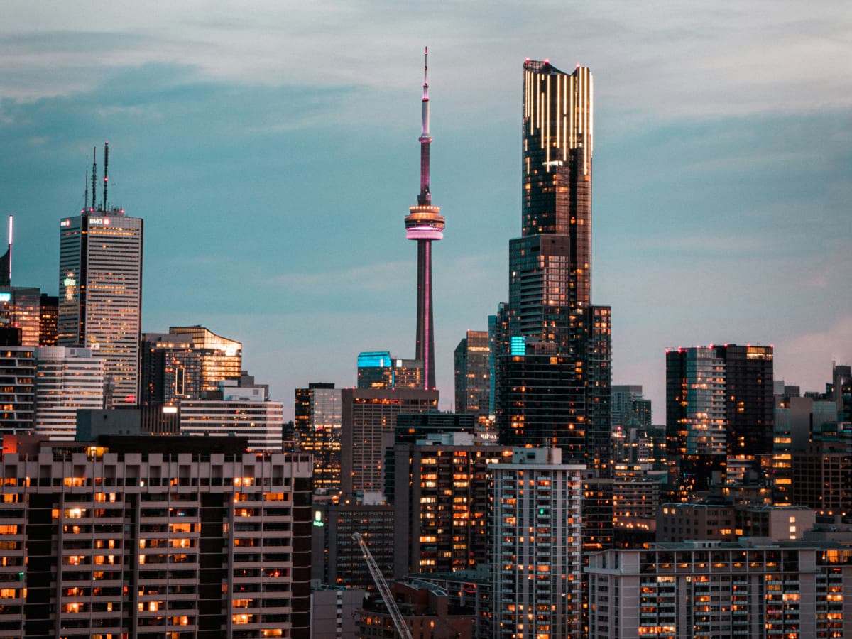 Toronto skyline at dusk with the CN Tower and surrounding skyscrapers illuminated against a blue-gray sky.
