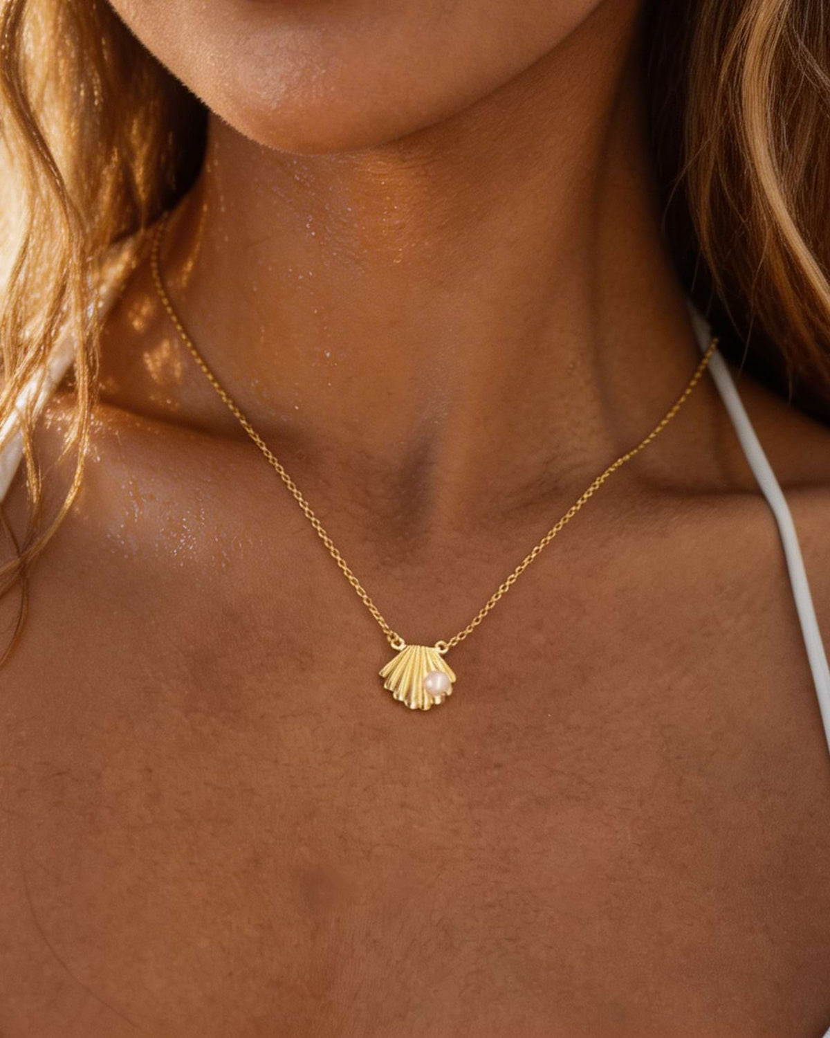 Gold necklace with a shell pendant on a person's neck