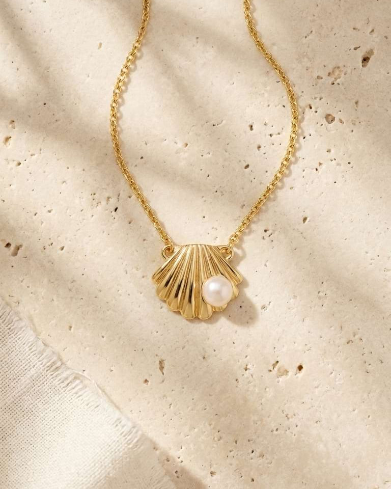 Gold necklace with a shell pendant and pearl on a textured beige surface